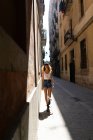 Очаровательная кудрявая женщина в шортах и жестоких сапогах, игриво стоящая на асфальтированной улице и развлекающаяся — стоковое фото