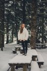 Dame blonde en veste blanche posant sur un pique-nique en bois en hiver et regardant la caméra — Photo de stock