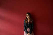 Young woman in jacket standing near red wall — Stock Photo