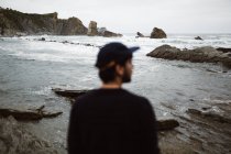 Vista trasera de un hombre borroso parado en la playa pedregosa y mirando hacia otro lado en Cantabria, España - foto de stock
