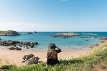 Donna in cappello seduta sull'erba sulla costa e godendo della vista sul mare nella giornata di sole — Foto stock