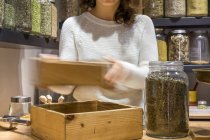 Crop unrecognizable woman with wooden box working in spice shop. — Stock Photo