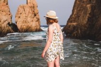 Visão traseira da mulher bonita segurando chapéu e em pé no oceano calmo na praia na baía — Fotografia de Stock