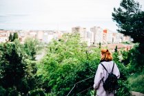 Женщина в футболке и рюкзаке в повседневной одежде наблюдает за городом из леса — стоковое фото