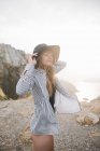 Junge Frau mit Hut steht am felsigen Ufer — Stockfoto