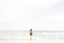 Mujer en traje elegante de pie cerca de la valla en el terraplén y disfrutando de la vista del mar - foto de stock