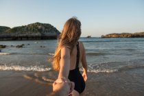 Junge Frau in Badebekleidung hält Hand des Mannes und geht zum winkenden Meer — Stockfoto