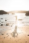 Силует жінки, що стоїть на мокрій піску біля моря в сонячний день — стокове фото