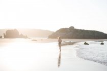 Silhouette di donna in piedi sulla sabbia bagnata vicino al mare nella giornata di sole — Foto stock