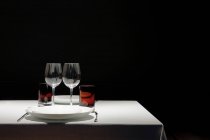 Tavolo rivestito con panno bianco pulito con vetri vuoti e piastre isolate su fondo nero — Foto stock