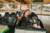 Joven mujer feliz montar coche de parachoques en el parque de atracciones divirtiéndose y mirando hacia otro lado - foto de stock
