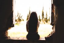 Charmante jeune femme admirant la nature assise dans une brèche dans le mur d'un bâtiment abandonné — Photo de stock