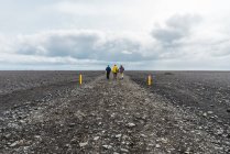 Vue arrière de touristes lointains marchant le long d'une belle route de gravier traversant une campagne pierreuse en Islande — Photo de stock