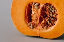 Saftige frische Hälfte des orangefarbenen Kürbisses mit Kernen und Fruchtfleisch auf grauem Hintergrund — Stockfoto