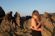 Bella giovane donna con gli occhi chiusi in piedi vicino alle rocce nella giornata di sole — Foto stock