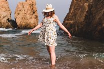 Красива жінка в капелюсі стоїть і розслабляється в океані на великих каменях — стокове фото