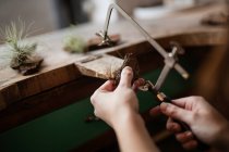 Руки крупным планом человека, вырезающего украшение куска коры дерева с инструментом на столе? — стоковое фото