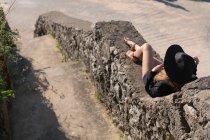 Donna in abito elegante e cappello sdraiato sul bordo antico in pietra nella giornata di sole e riposo — Foto stock
