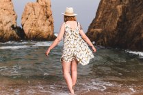 Jolie femme en chapeau debout et relaxant dans l'océan à de gros rochers — Photo de stock