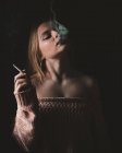 Attrayant jeune femme sensuelle fumant la cigarette sur fond sombre. — Photo de stock
