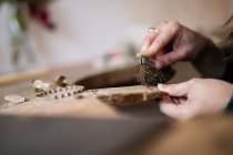 Обрезание крупными руками женской резьбы и чистка мелких деталей кисточкой за столом — стоковое фото