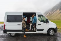 Двоє молодих чоловіків стоять біля гарного білого фургона, подорожуючи мальовничою ісландською місцевістю. — стокове фото