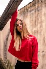 Casual young blonde in red hoodie standing with hand up on grungy background looking sensually at camera. — Stock Photo