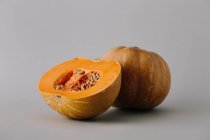 Jugosa calabaza de naranja fresca con la mitad sobre fondo gris - foto de stock