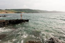 Donna in costume da bagno in piedi su roccia in mare e guardando la vista — Foto stock