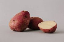 Batatas frescas inteiras e cortadas pela metade no fundo cinza — Fotografia de Stock
