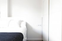 Cómoda cama de pie cerca del armario en el cuarto de luz agradable. - foto de stock