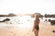 Silhouette de femme debout sur du sable humide près de la mer par une journée ensoleillée — Photo de stock