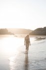 Unerkennbare Frau läuft im Sonnenlicht auf Sand am Meer — Stockfoto