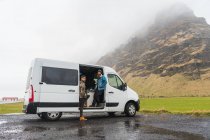 Dois jovens que estão perto de uma bela van branca enquanto viajam através do magnífico campo islandês — Fotografia de Stock