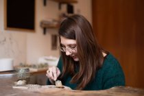Обрізати крупним планом руки жінки різьблення дерев'яні деталі з ножем за столом — стокове фото