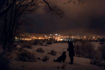 Homem e seu animal de estimação caminham à noite na floresta nevada em um inverno próximo — Fotografia de Stock