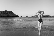 Vista posteriore donna in costume da bagno nero in piedi vicino al mare — Foto stock