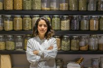 Pretty shop assistant woman standing with arms crossed at shelves with spices. — Foto stock