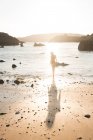 Silhouette di donna in piedi su sabbia bagnata vicino al mare in retroilluminazione — Foto stock