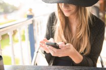 Frau im eleganten Outfit sitzt mit Smartphone am Tisch — Stockfoto
