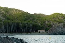 Piccola baracca in piedi vicino a montagna e foresta sulla bellissima costa di Tavallera — Foto stock