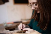 Обрізати крупним планом руки жінки різьбленням і чистити дрібні деталі пензлем за столом — стокове фото