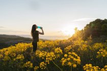 Side view of female drinking water from bottle standing at sunset on picturesque backlit background of El Montcau in Barcelona, Spain — Stock Photo