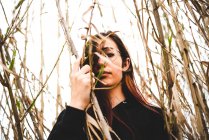 Таємнича дівчина в чорному вбранні, що стоїть у високій сушеній траві і дивиться на камеру — стокове фото