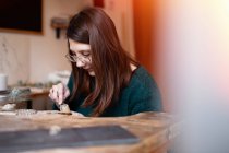 Recadrer fermer les mains de la femme sculptant détail en bois avec couteau au bureau — Photo de stock