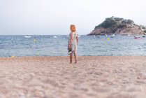 Seitenansicht einer Frau, die Sandalen trägt, während sie am Sandstrand am Meer spaziert — Stockfoto