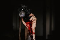 Crop shot of tattooed hand holding photo camera with thick dark blood running down on black background — Stock Photo