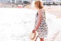 Rückansicht einer hübschen Frau mit Hut, die am ruhigen Meer am Strand in der Bucht steht — Stockfoto