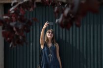 Jovem mulher sorrindo e posando para selfie enquanto está perto de cerca — Fotografia de Stock