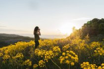 Donna che scatta foto in montagna con fiori gialli — Foto stock